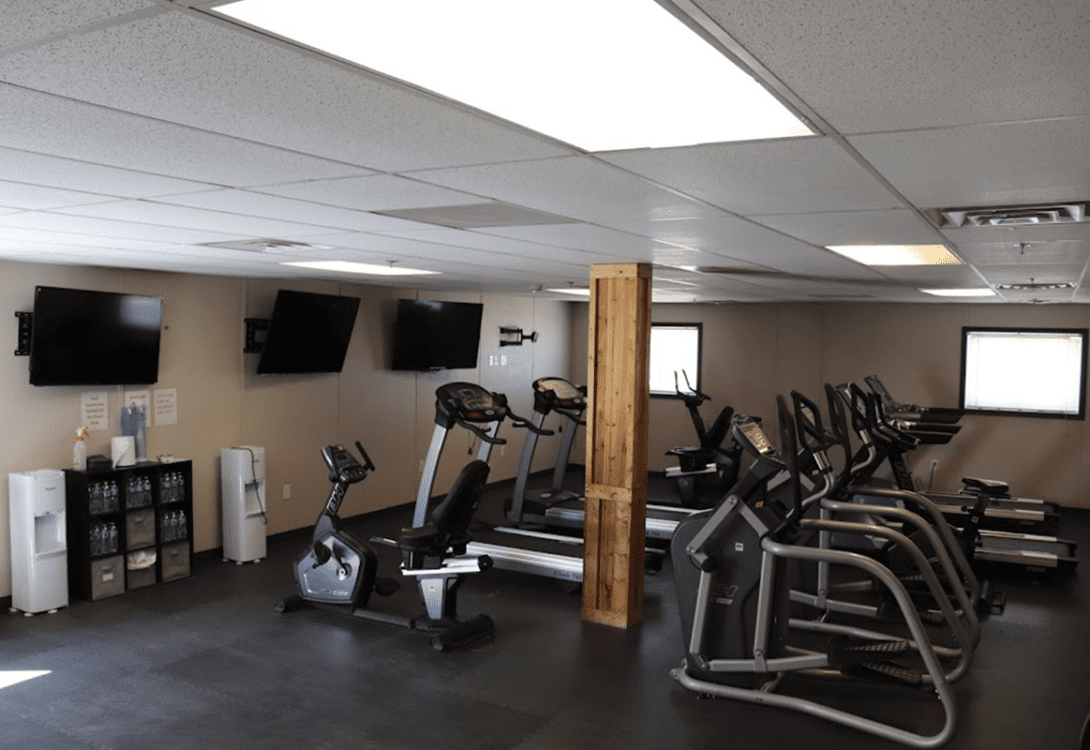 The workout room in CHH Orla Lodge, with several treadmills, water station and three flat screens mounted in the wall